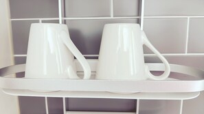 Dos tazas blancas sobre una bandeja frente a una pared de azulejos.