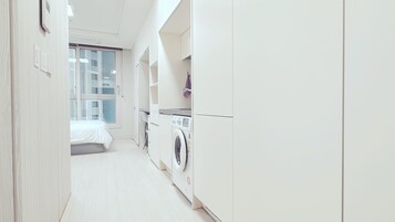 A modern, white-walled bedroom with a large window, a washing machine, and a bed.