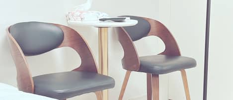Two modern chairs with wooden and leather design, a small round table with a tissue box, and a white wall.