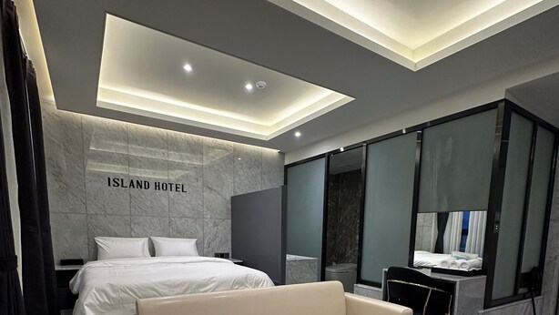 A modern hotel room with a large bed, a sofa, a marble coffee table, and a desk. - Hotel Island (Ansan)