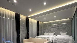 A modern hotel room with a marble floor, a beige sofa, two beds, and a wall-mounted sign that reads "ISLAND HOTEL". - Hotel Island (Ansan)