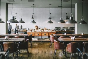 Een ruim restaurant met houten tafels en stoelen, een centraal eiland met keukengerei, en hangende industriële hanglampen.