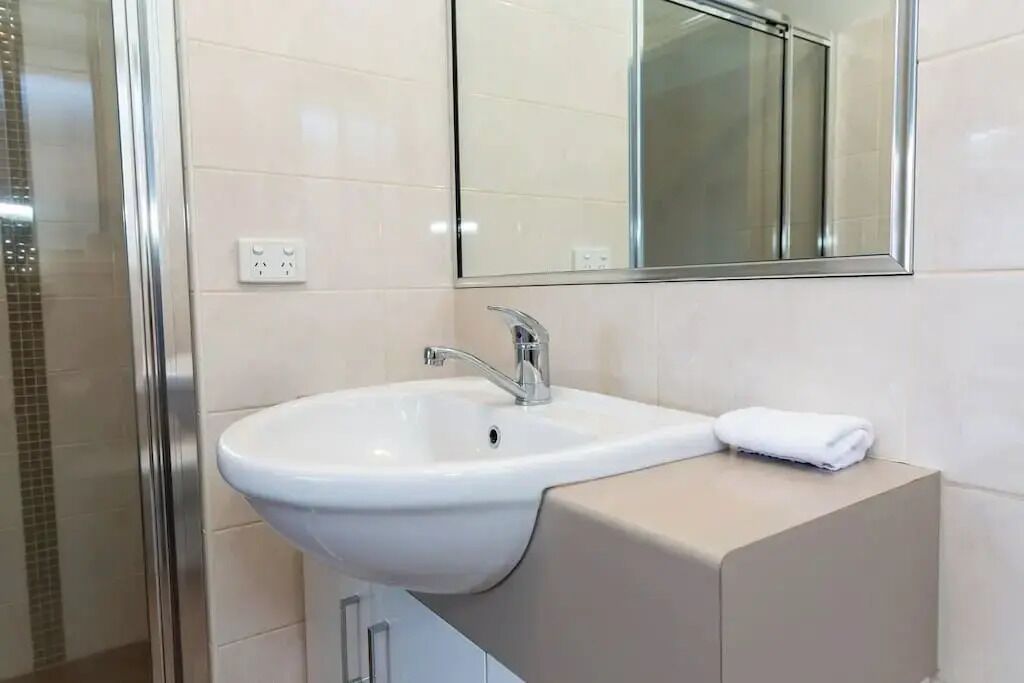 Ein Badezimmer mit einem weißen Waschbecken, einem Spiegel und einem Handtuch auf einem beigen Schrank.
