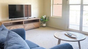 Una sala de estar con un televisor sobre un mueble de madera, una planta en maceta y una mesa de centro redonda.
