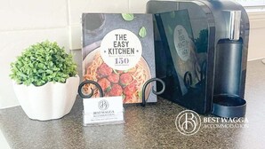 Un espacio de cocina con un libro titulado “The Easy Kitchen 150 Great Recipes”, un cartel de Best Wagga Accommodation y una cafetera negra.