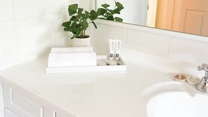 A white bathroom vanity with a sink, a potted plant, and toiletries. - Modern Parkview Retreat, a bright & well-maintained apartment in prime location! (Wagga Wagga)