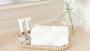 A bathroom vanity with a white towel, two tubes of cream, and a vase with an orchid. - Modern Parkview Retreat, a bright & well-maintained apartment in prime location! (Wagga Wagga)