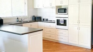 A modern kitchen with white cabinetry, a wooden countertop, and a microwave. - Modern Parkview Retreat, a bright & well-maintained apartment in prime location! (Wagga Wagga)