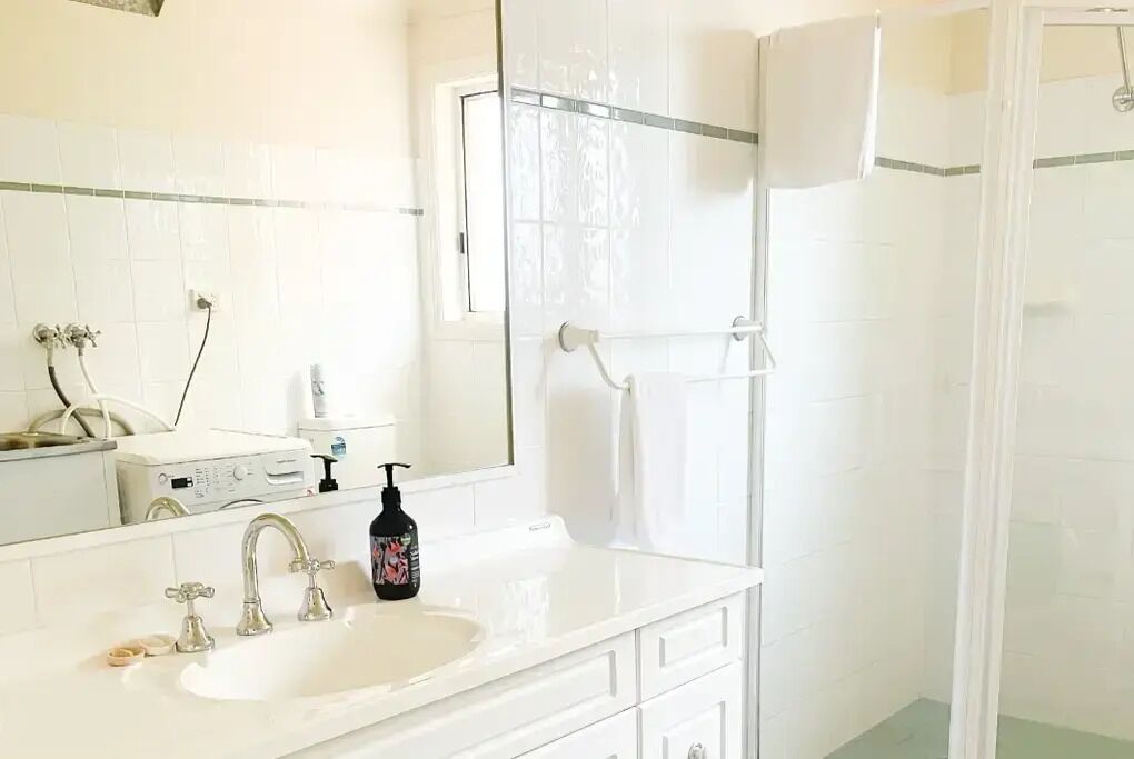 Une salle de bain avec un lavabo blanc, deux robinets, un miroir et un espace douche séparé par un rideau.