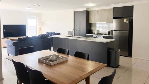 A modern kitchen with a central island, dark cabinetry, and stainless steel appliances. - Welcome to our stylish 3BR villa, perfect for an escape (Wagga Wagga)