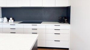Een moderne keuken met witte kasten, een zwarte achterwand en een koffiezetapparaat.