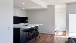 Een moderne keuken met een wit aanrecht, zwarte barstoelen en een zwarte achterwand.