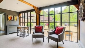 A room with large windows, a fireplace, two armchairs with red cushions, and a table. - Idyllic Cottage in the heart of The South Downs (Haslemere)