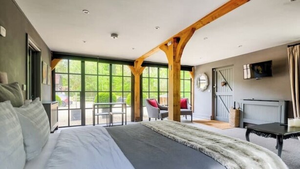 A bedroom with a large bed, wooden beams, a view through the window, and a small table with chairs. - Idyllic Cottage in the heart of The South Downs (Haslemere)