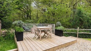 A wooden deck with a table and chairs, surrounded by greenery and a wooden fence. - Idyllic Cottage in the heart of The South Downs (Haslemere)