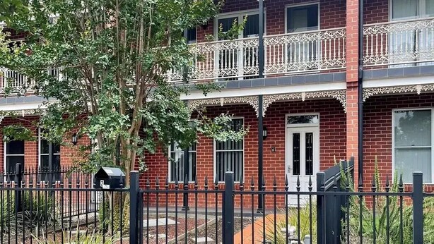 A two-story brick building with a balcony, a gated entrance, and a small garden area. - Discover urban living in our contemporary townhouse! (Wagga Wagga)