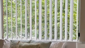 A bedroom with a bed, pillows, a bedside table with a lamp, and a window with vertical blinds. - Discover urban living in our contemporary townhouse! (Wagga Wagga)