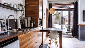 A modern kitchen with a wooden countertop, stainless steel appliances, and a dining area with a white chair.