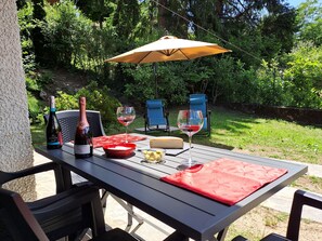 An outdoor dining area with a table, chairs, a bottle of wine, glasses, and a cheese board. - Detached, cool, sunny and quiet cottage with large garden (Magreglio)