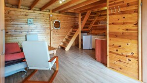 A cozy log cabin interior with a wooden staircase, a dining area with a table and chairs, and a kitchenette.