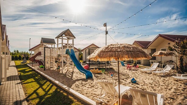 A beachside resort with a playground, beach chairs, and thatched umbrellas.