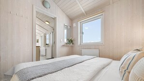A bedroom with a large bed, a window, a mirror, and a shelf with flowers. - Cozy vacation home Harzer Nest with sauna, terrace and panoramic view in the Harz Mountains (St. Andreasberg)