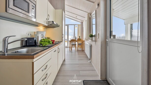 A narrow kitchen with a microwave, sink, and wooden cabinets. - Cozy vacation home Harzer Nest with sauna, terrace and panoramic view in the Harz Mountains (St. Andreasberg)