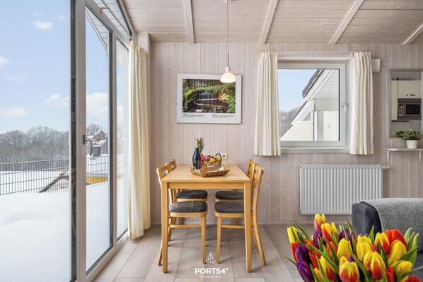 Ein Essbereich mit Holztisch, Stühlen, einem gerahmten Bild und einem Fenster mit Blick auf eine verschneite Landschaft.