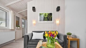 A modern living room with a grey sofa, a wooden coffee table with a book and a vase of tulips, a framed picture on the wall, and a small wooden side table with a plant. - Cozy vacation home Harzer Nest with sauna, terrace and panoramic view in the Harz Mountains (St. Andreasberg)