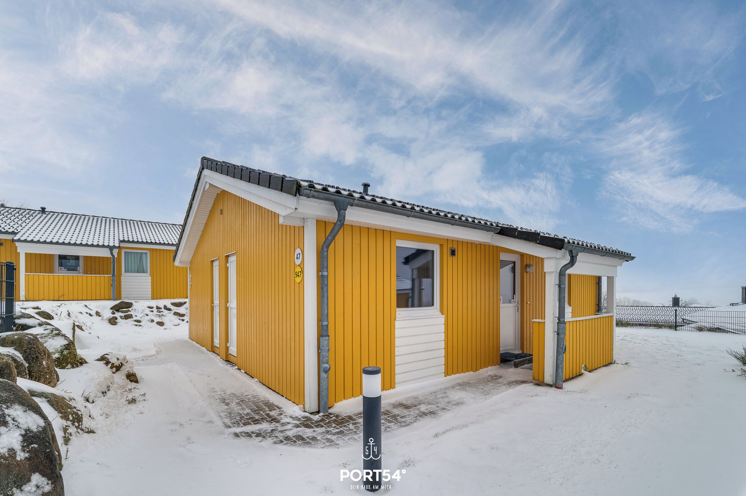 Un bâtiment jaune avec une porte et une fenêtre blanches, un petit porche et un sol recouvert de neige.