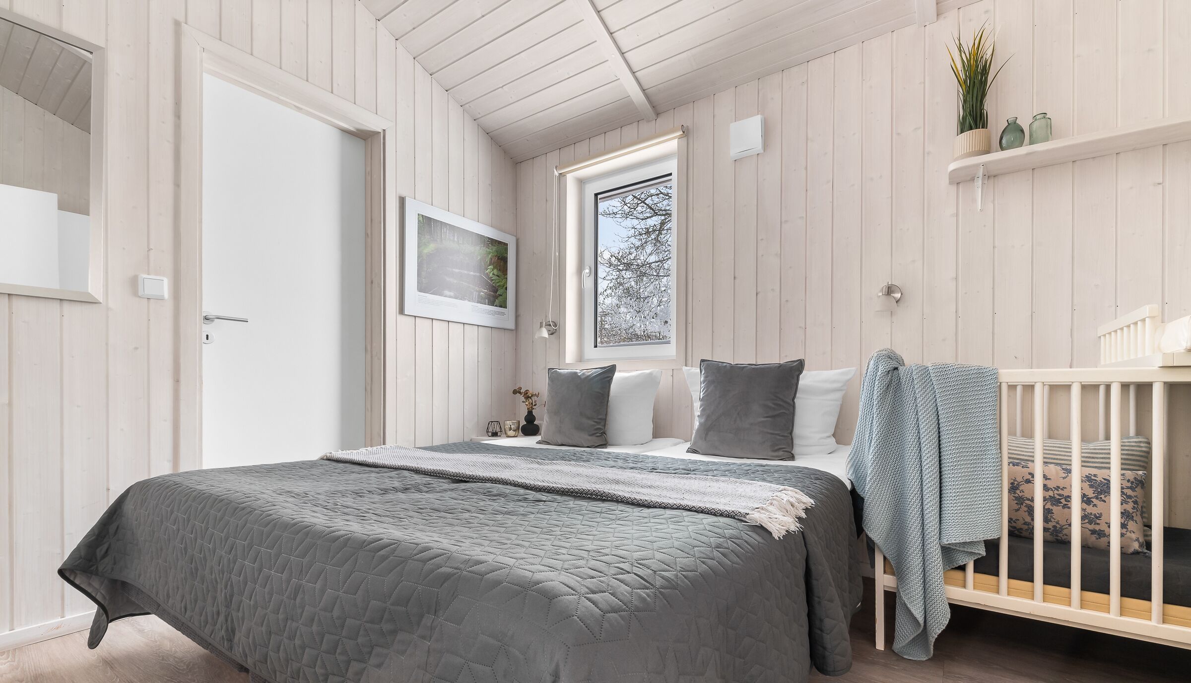 A bedroom with a bed, a crib, a window, and a shelf with plants.