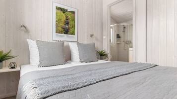 Une chambre à coucher avec un lit, des oreillers, un tableau encadré, une plante sur la table de chevet et un espace douche.