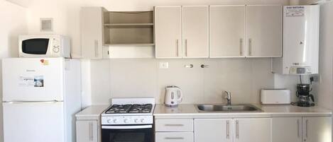 A compact kitchen with white cabinets, a gas stove, a microwave, a refrigerator, a sink, and a coffee maker.