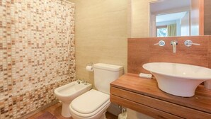 A bathroom with a mosaic shower curtain, a toilet, a bidet, and a wooden vanity with a sink.