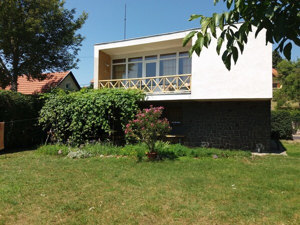 A modern two-story house with a balcony, surrounded by a well-maintained garden with various plants and flowers.