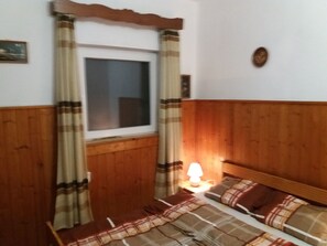 A bedroom with a wooden headboard, a window with curtains, a bedside lamp, and a bed with a plaid blanket.