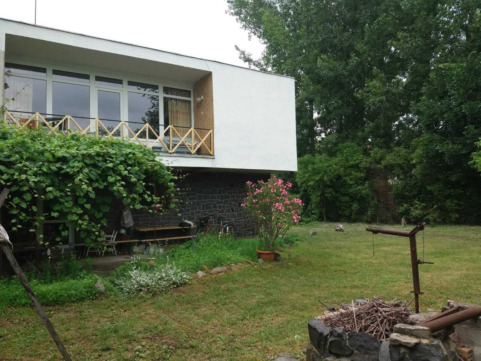 A modern two-story house with a stone foundation, a wooden deck, and a garden with a fire pit.