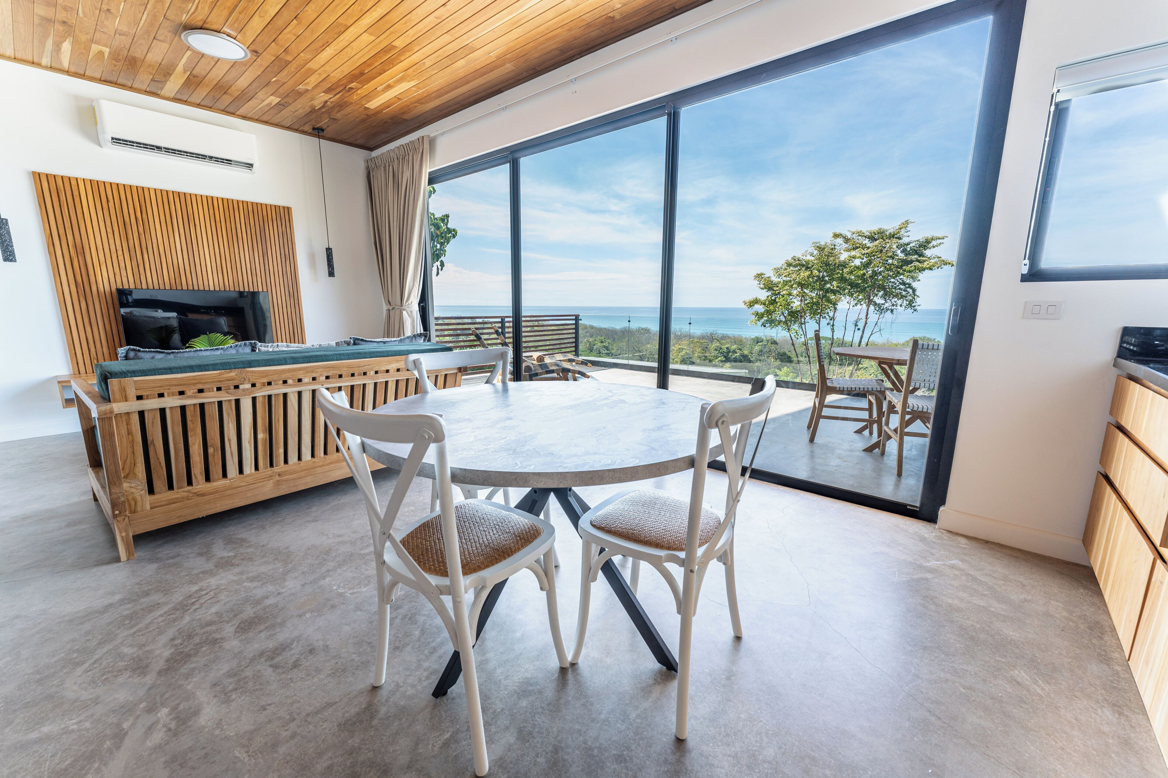 Une cuisine moderne avec un plafond en bois, une grande fenêtre donnant sur un paysage magnifique et un coin repas avec des chaises blanches.