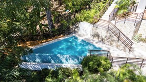 A swimming pool surrounded by lush greenery and stone walls, with a wooden staircase leading up to a white building. - Sea View Paradise Retreat by Sea N' Rent (Cóbano)