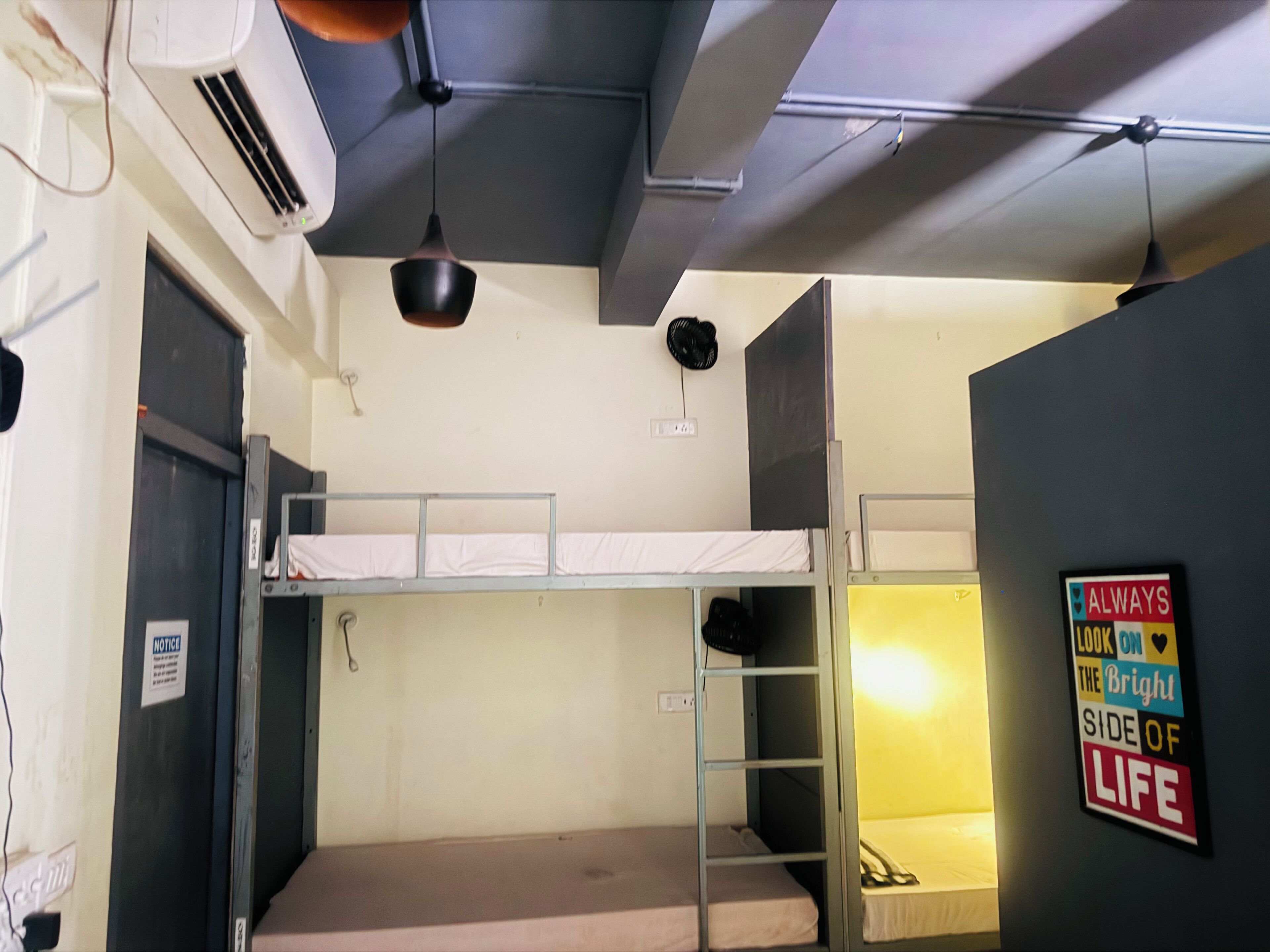 A dormitory room with bunk beds, a notice board, an air conditioning unit, and a motivational poster.