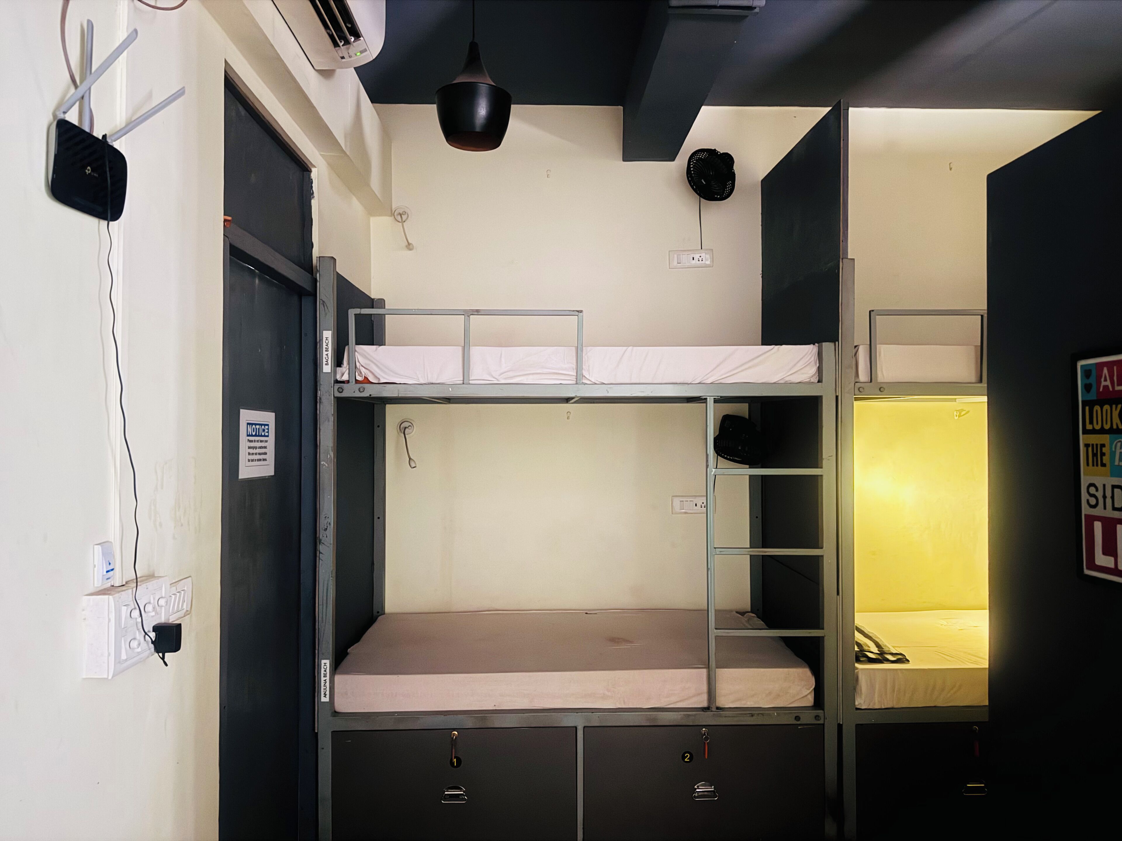 A bunk bed room with a desk and a chair, a wall socket, and a notice sign.