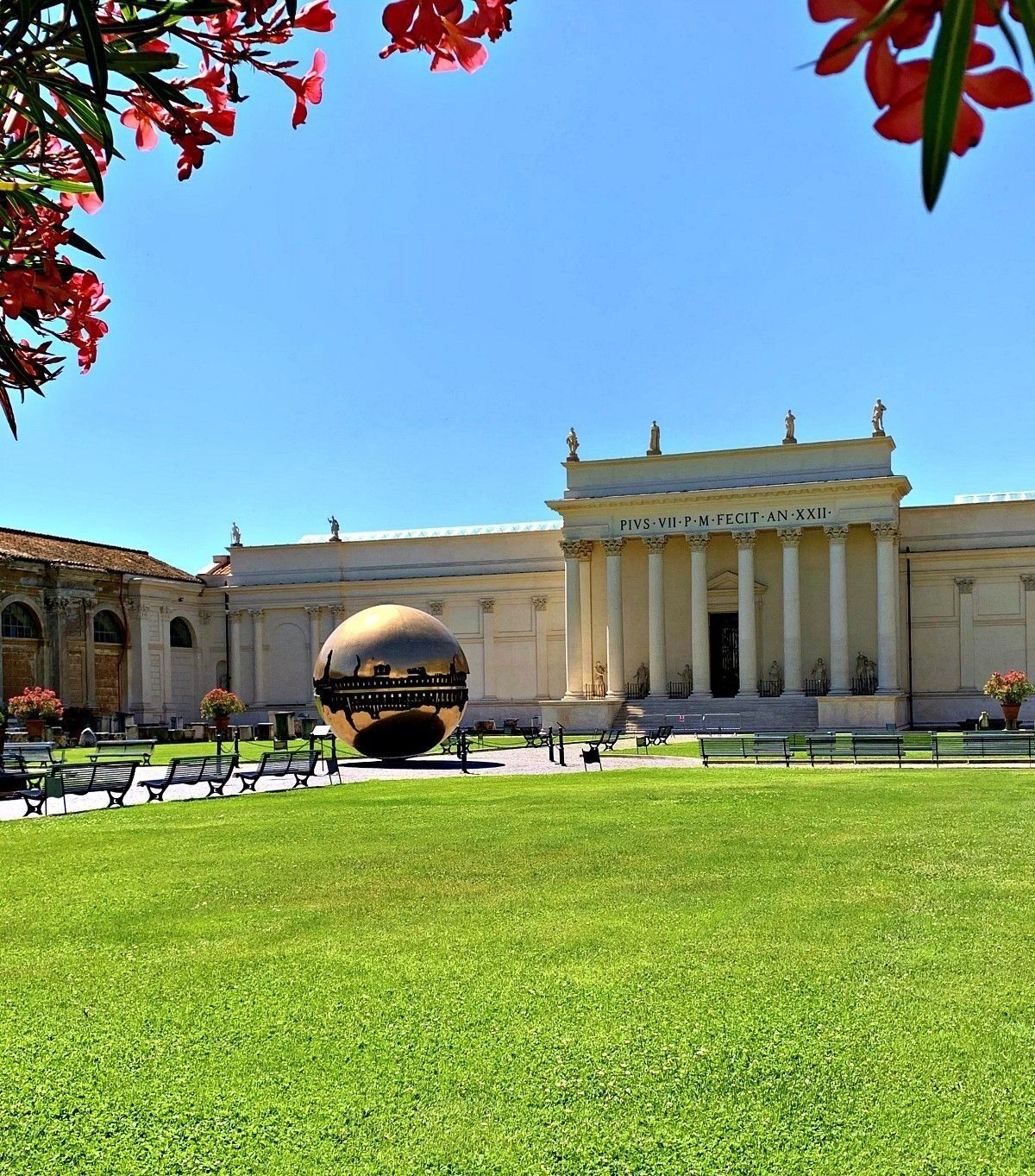 A large spherical sculpture in front of a classical building with columns and a sign reading "PIVS-VII-P.M.FECIT-XXII."