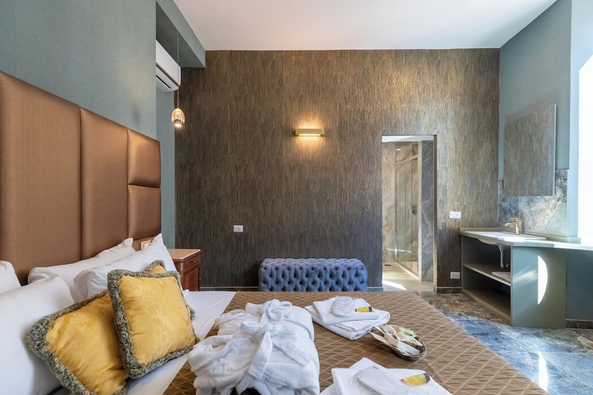 Een hotelkamer met een groot bed, een blauwe gestoffeerde bank, een badkamer met een marmeren wastafel en een wandlamp.