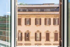 Fachada de edifício com janelas e persianas uniformemente distribuídas, varanda com grades em treliça e céu claro ao fundo.