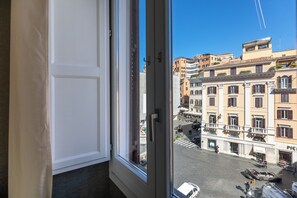Vista da janela com porta branca, sobre um quarteirão com edifícios e céu limpo.