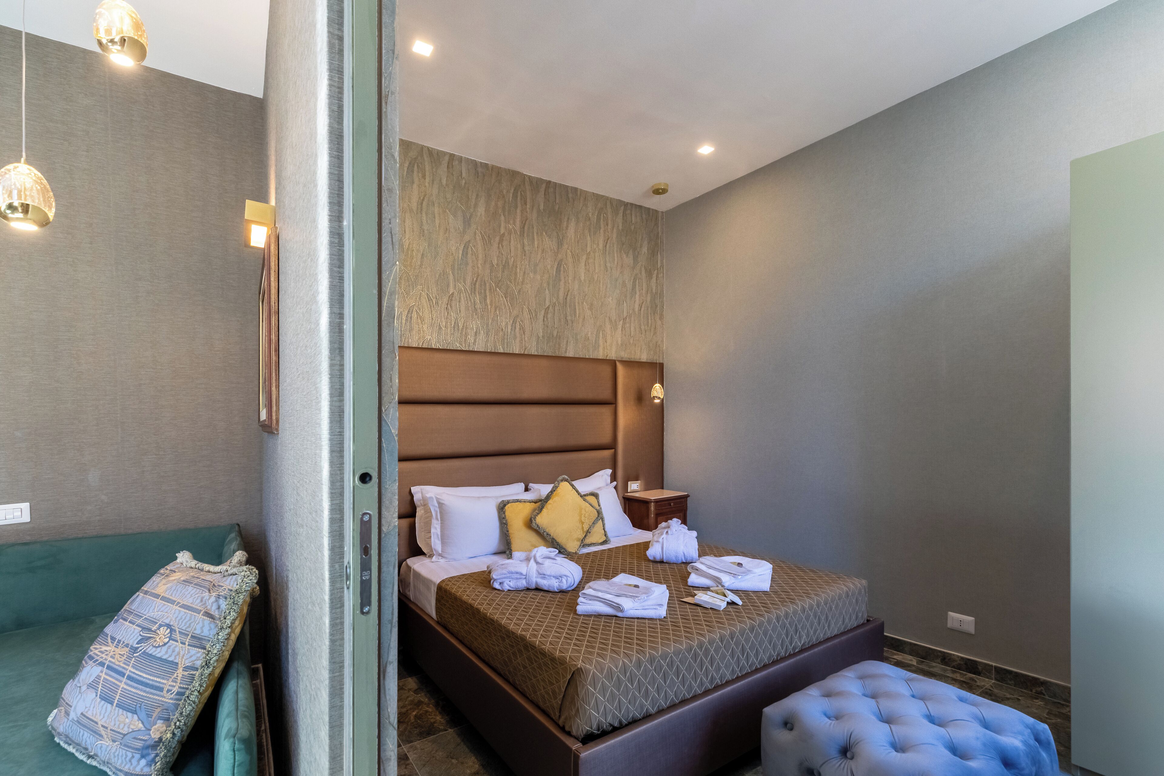 A modern hotel room with a large bed, a green sofa, and a tufted ottoman.