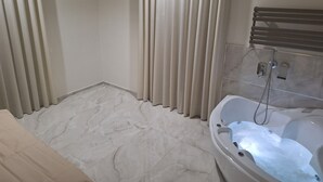 Un baño con piso de mármol, una bañera con agua corriendo y un perchero para toallas.
