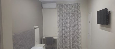 A bedroom with a bed, a desk, and a shower area.