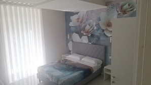 Un dormitorio con cama, mesita de noche, armario y pared con un mural floral.