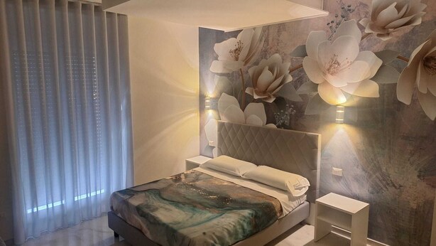 Un dormitorio moderno con una cama grande, una mesita de noche y una pared decorada con motivos florales.